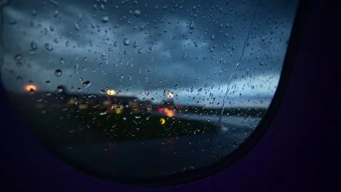 Close-up of raindrops on an airplane window at dusk with blurred airport lights Stock Footage 342276742