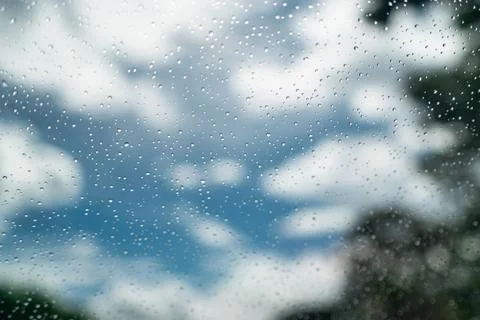 Close up of raindrops on clear glass window against cloudy blue sky. Stock Photos
