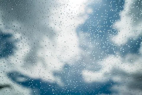 Close up of raindrops on clear glass window against cloudy blue sky. Stock Photos