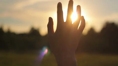Close-up of raised hand in the sky against the sun in nature, religion Stock Footage