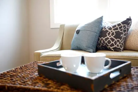 Close up of rattan trunk coffee table with a wood tray and white cups next to Stock Photos