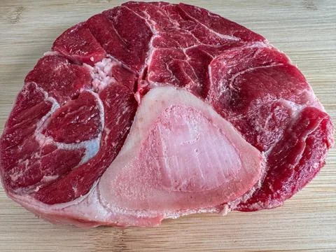 Close-up of raw beef shank cross-cut with visible bone, placed on a wooden cu 스톡 사진