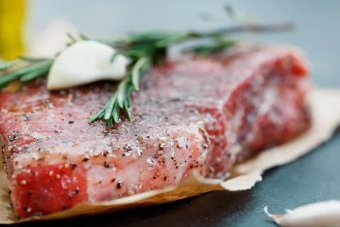 Close-up of raw beef steak on craft paper with garlic and rosemary. Cooking Stock Photos