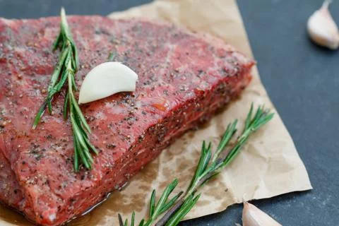 Close-up of raw beef steak on craft paper with garlic and rosemary. Cooking Stock Photos