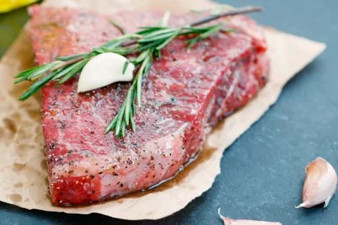 Close-up of raw beef steak on craft paper with garlic and rosemary. Cooking Stock Photos