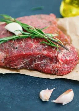 Close-up of raw beef steak on craft paper with garlic and rosemary. Cooking Stock Photos