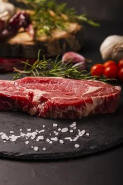 Close up of raw beef steak on slate background with salt and herbs. Stock Photos