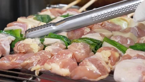 Close-up of raw chicken and green onion yakitori skewers being seasoned with sal Stock Footage 337440753