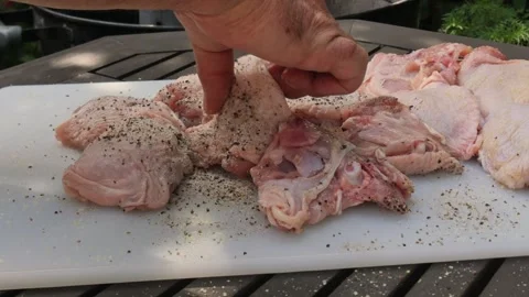Close-up of raw chicken thighs being prepared for a backyard BBQ with herbs.. Vidéo 337410270
