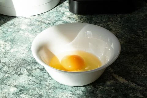 Close-up of a raw, cracked chicken egg in a white plate on a kitchen table Stock Photos