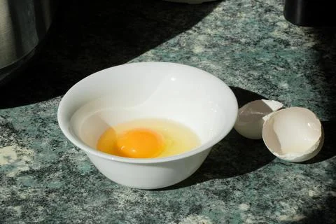 Close-up of a raw, cracked chicken egg in a white plate on a kitchen table Stock Photos