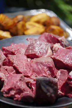 Close up of raw diced beef meat pieces on a foil plate and roasted potato in the Stock Photos
