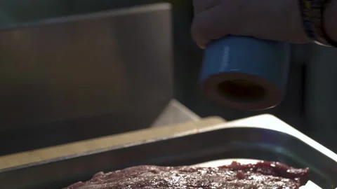 Close-up of raw meat lying on metal protvin, which peppered with pepper grinder Stock Footage 153383778