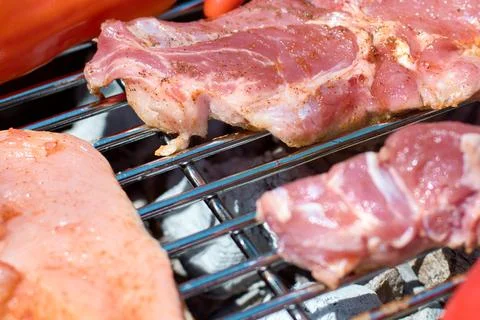 Close-up of raw pork meat cuts sizzling on a hot metal barbecue grill grate Stock Photos