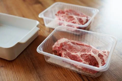 Close-up of raw pork steak in plastic tray on wooden surface Stock Photos