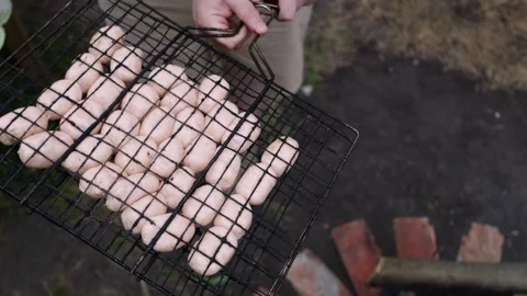 Close-up of raw sausages being grilled over an open fire in a barbecue basket Stock Footage 337105311