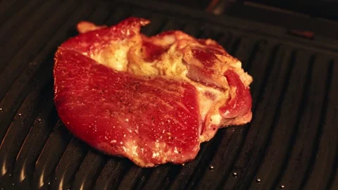 Close-up of raw seasoned steak sizzling on a hot grill pan Stock Footage 340562753