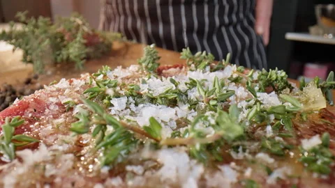 Close-up of a raw steak being sprinkled with salt by a chef. Slow motion 50fps. Stock Footage 305385981