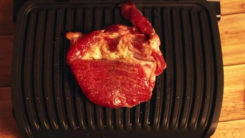 Close-up of raw steak cooking on a black electric grill with wooden background Vidéo 340562694