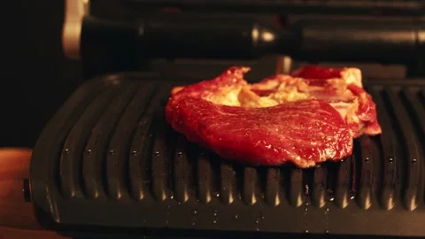 Close-up of raw steak cooking on an electric grill with warm lighting Stock Footage 340562718