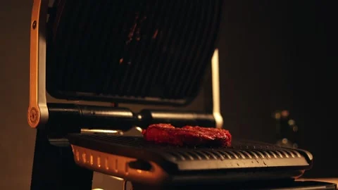 Close-up of raw steak cooking on a modern electric grill indoors Stockbeeldmateriaal 340562826