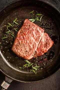 Close up raw wagyu beef striploin steak with pepper on dark pan. Restaurant Stock Photos