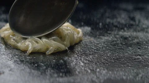Close up of raw whitebait slowly poured and spread onto hot plate for cooking Stock Footage 89994339
