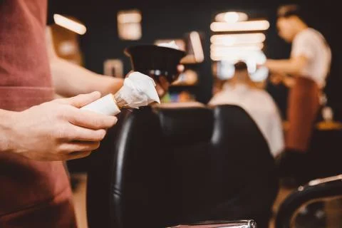 Close-up razor in hands of barber, background client is waiting for shaving Stock Photos