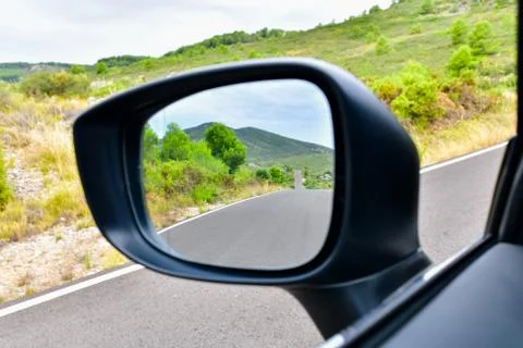 Close up of a rear view mirror with an empty road with mountains at the back Stock Photos