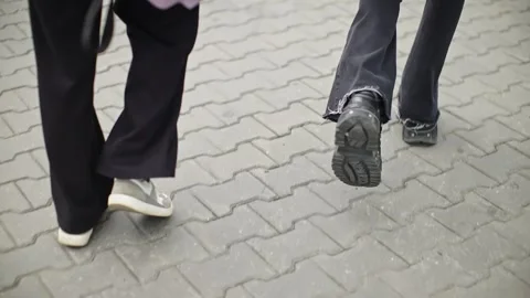 Close-up rear view of two people walking side by side on an urban paved sidewalk Stock Footage 326064662