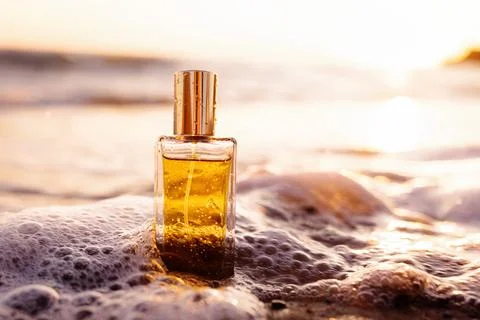 Close up of rectangular glass bottle with golden perfume washed by sea surf.  Foto stock
