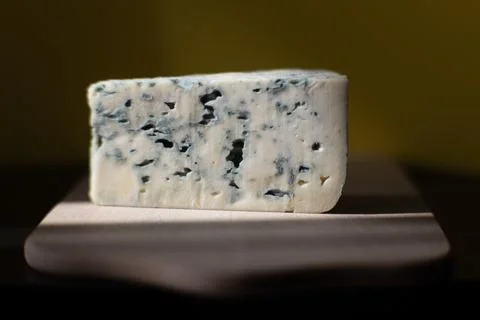 Close-up of a rectangular piece of blue cheese on a wooden board with soft .. Stock Photos