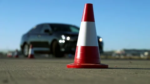 Close-up of red and white road cone with black car passing barriers. Unknown Stock Footage 148748589