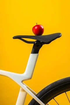 Close up of red apple placed on black saddle of white bicycle on bright yello Stock Photos