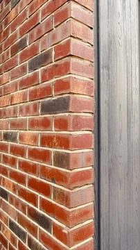 Close-up of a red brick wall corner adjacent to grey wooden siding with vis.. Stock Photos