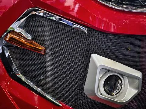 Close-up of a red car front with a grille, fog light, and design details in.. 스톡 사진