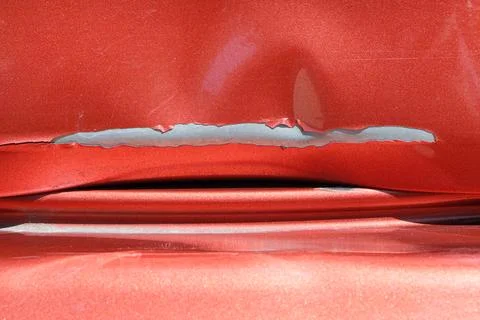 Close up of a red car with multiple visible scratches and paint damage. The Stock Photos