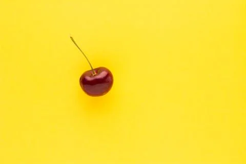 Close up of a red cherry and stem against a yellow background Stock Photos