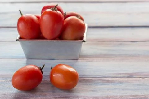 Close up red cherry plum tomatoes in stainless bowl on wood table background Stock Photos