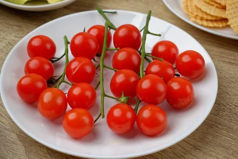 Close-up of red cherry tomatoes on branches on a white plate. Stock Photos