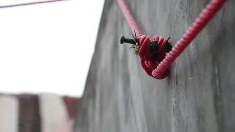 Close-Up of Red Clothesline Rope Tied to Wall Anchor on Concrete Surface Stock Footage 336983406