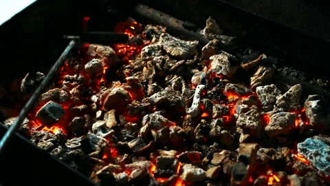 Close up of red coals being mixed by black rake in barbeque, slow motion. Video stock 87322662