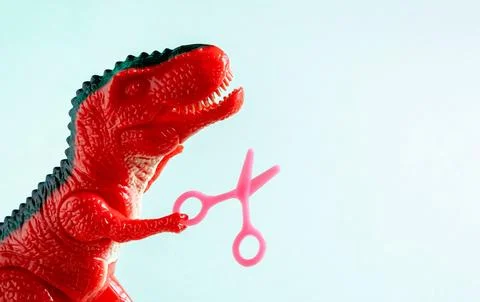 Close up red dinosaur holding tiny scissors. Beauty care, hairdressing concep Foto stock