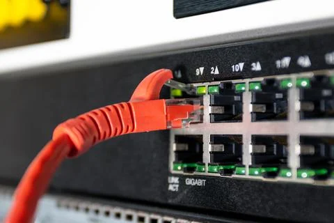 Close up of red ethernet cable plugged into network switch, showing wired i.. Photos
