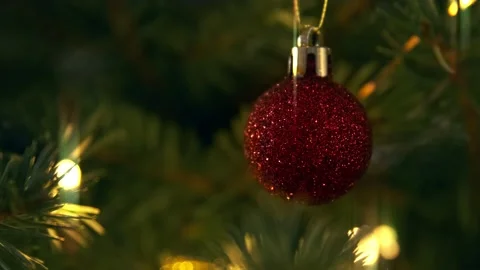 Close up of red glitter ball swinging in motion with ligts on christmas tree Stock Footage 145272225
