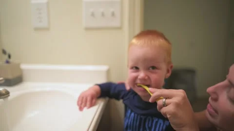 Close-up of red-haired toddler smiling while parent helps him brush his teeth Stockbeeldmateriaal 295837970