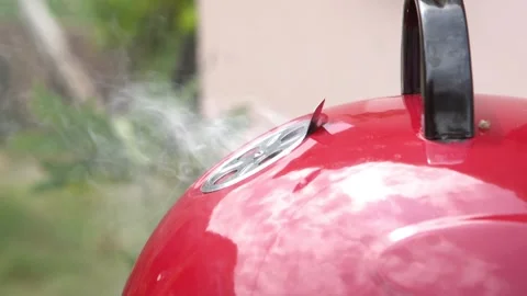 Close-up of a red kettle BBQ smoker releasing smoke through the lid vent during Stock Footage 337892306