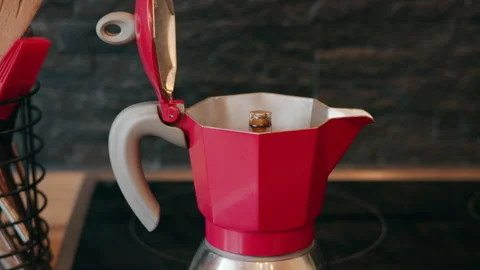 Close-up of a red moka pot coffee maker with open lid, standing on a stovetop in Видео 331170920