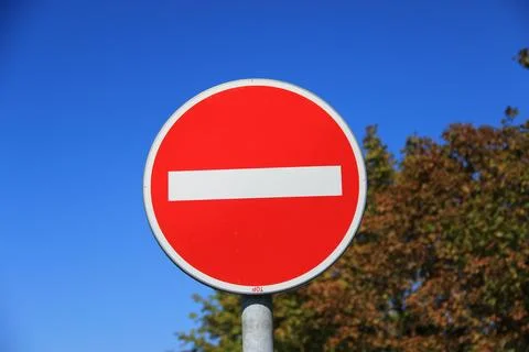 Close-up of a red no entry traffic sign against a clear blue sky with trees.. Fotos Stock