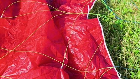 Close up of a red paraglider canopy spread across green grass, with bright Stock Footage 337505563